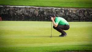 Golfer crouches on a lush green, showing concentration in golf while planning a putt